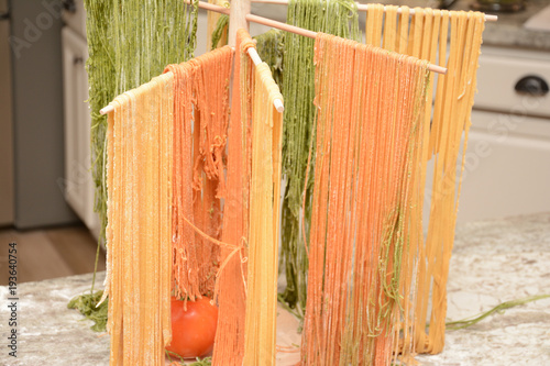 Colorful red and green fresh made pasta drying on wooden tree rack