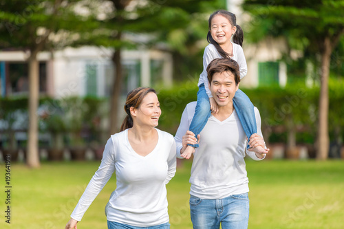 Cute Asian girl on neck parents big happy laughing and run around together.Happy family piggybacking adorable little daughter is smiling.