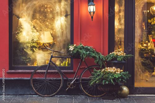 Christmas decorated showcase with old bicycle, fir branches, glass shiny toys and vintage lantern. Red building facade