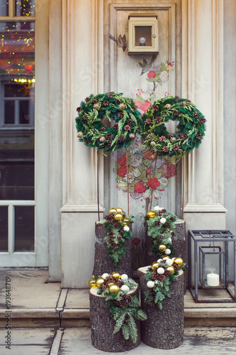 Facade decoration with christmas wreaths with fir branches and cones. Greeting arrangement on entrance with beautiful New Year toys