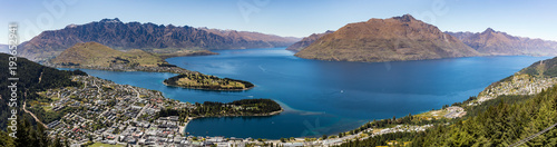 A panoramic landscape of Queenstown, New Zealand with Lake Wakatipu under a blue sky