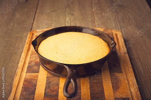 Fresh from the oven corn bread on wooden chopping board and cast iron pan.