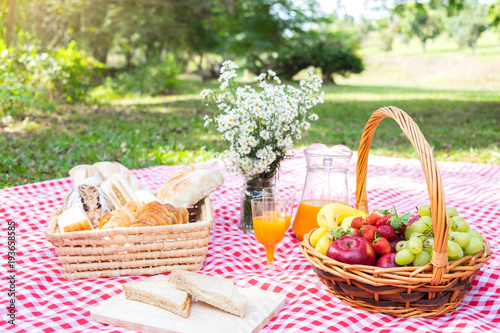 Fototapeta Naklejka Na Ścianę i Meble -  Healthy food and accessories outdoor summer or spring picnic, Picnic wicker basket with fresh fruit, bread and a glass of refreshing orange juice in the camping nature background