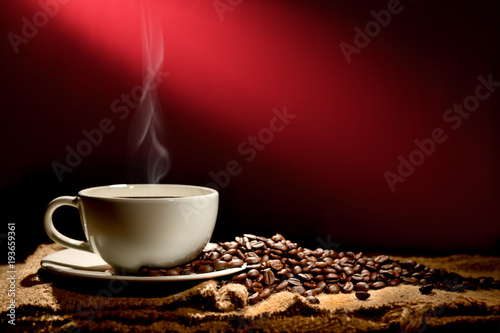 Cup of coffee with smoke and coffee beans on reddish brown background