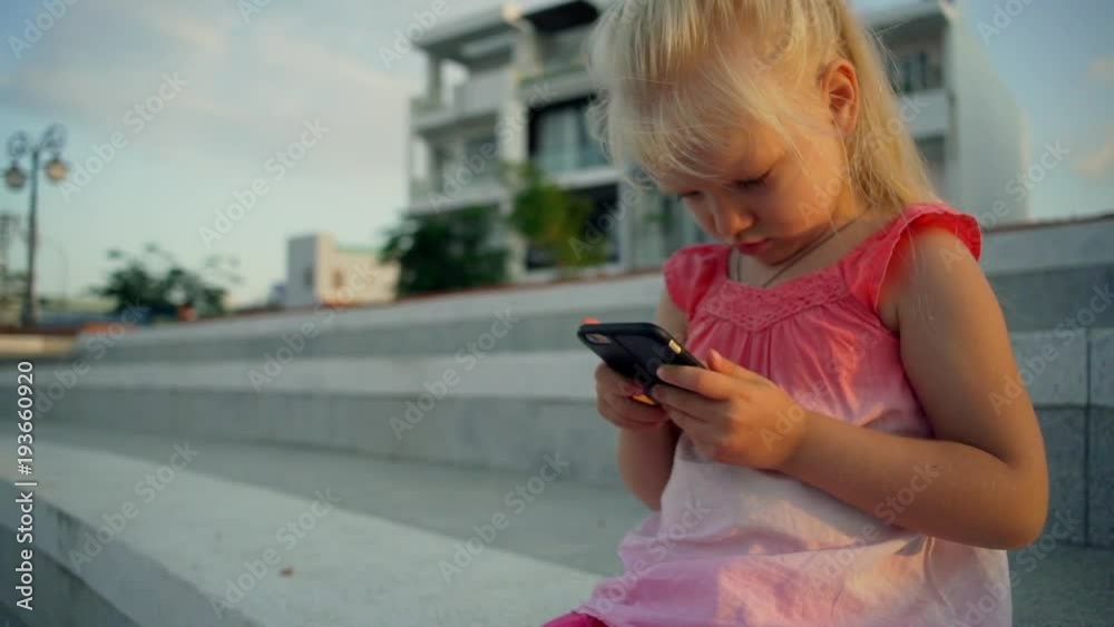 Blonde baby girl use smartphone in the park at sunset rapid slow motion Blonde baby girl use smartphone in the park at sunset rapid slow motion