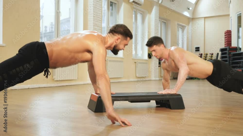 Two male athletes clenches their fists relying on the step in the gym