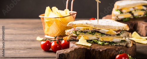 Fresh club sandwich with ham, cheese, boiled eggs and potatoes chips on wooden background. Healthy fast food concept with copy space. Banner.