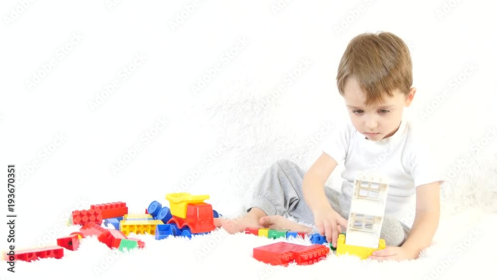 Happy child playing in colored blocks, sitting on white background. A child is playing on the couch. Motion camera slider. Happy child playing in colored blocks, sitting on white background. A child is playing on the couch. Motion camera slider.