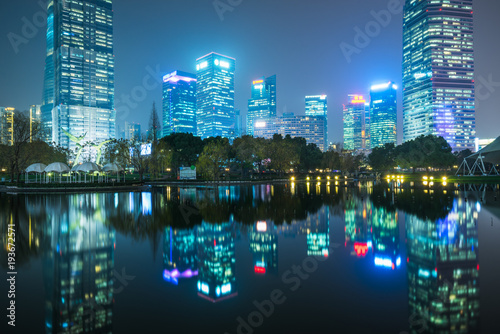illuminated modern skyscrapers standing by park lake at night shanghai china.