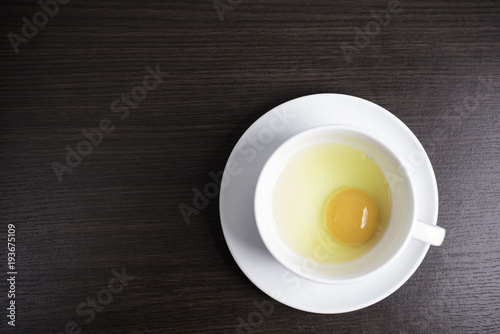 Fresh egg in white cup on wood background.