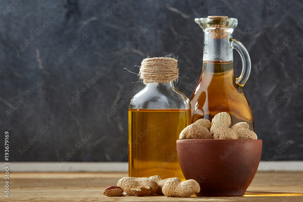 Aromatic oil in a glass jar and bottle with peanuts in bowl on wooden table, close-up Aromatic oil in a glass jar and bottle with peanuts in bowl on wooden table, close-up
