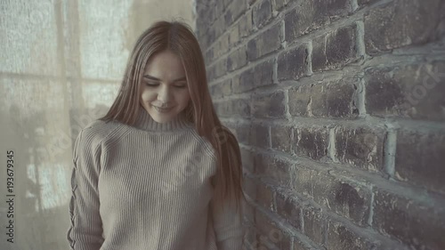 Portrait of young caucasian woman walks along the brick brown wall in studio. Brunette Girl is dressed in a beige sweater.