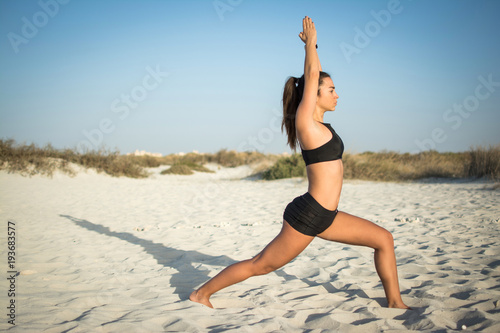 Slim young woman doing yoga in low lunge pose on the beach.