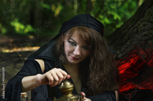 young witch from legends and fairy tales performs a sorcerous rite in the forest.