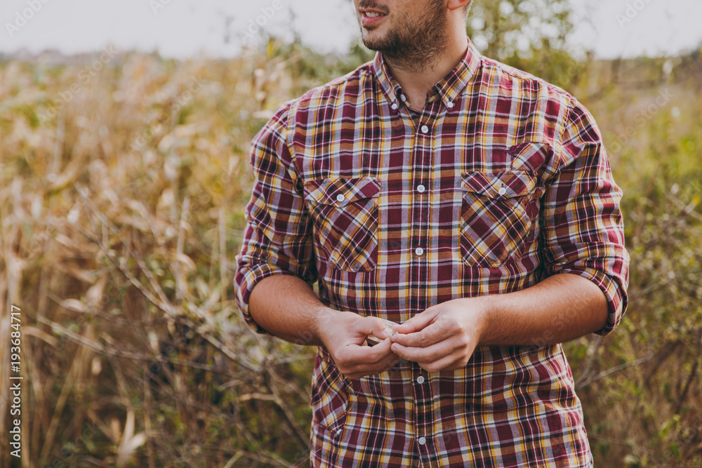 Close up cropped young unshaven man in checkered shirt turned his head and holds maggot bait for fishing against the background of shrubs and reeds. Lifestyle, fisherman recreation, leisure concept. Close up cropped young unshaven man in checkered shirt turned his head and holds maggot bait for fishing against the background of shrubs and reeds. Lifestyle, fisherman recreation, leisure concept.