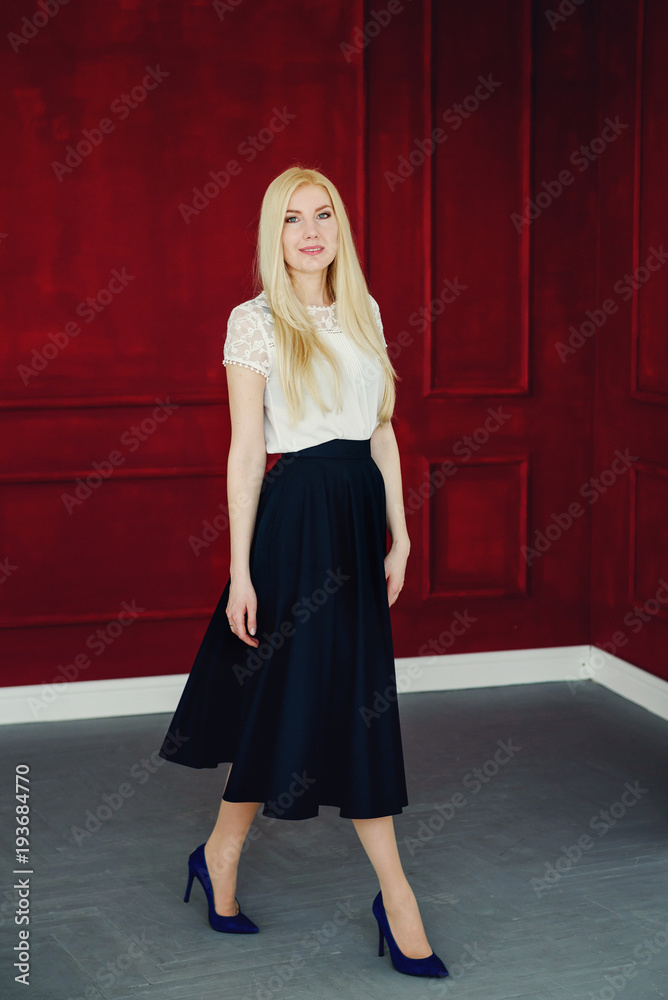 Full length portrait of a beautiful blonde girl in black white clothes on the burgundy studio background