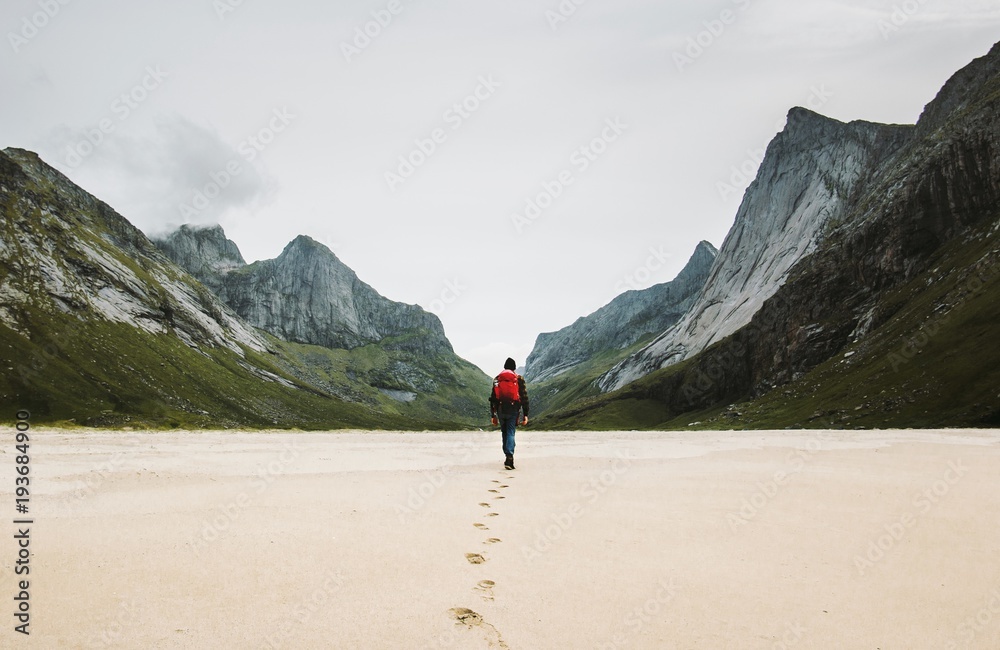 Man with backpack walking away alone at sandy beach in mountains Travel lifestyle concept adventure outdoor summer vacations in Norway wild nature - obrazy, fototapety, plakaty 