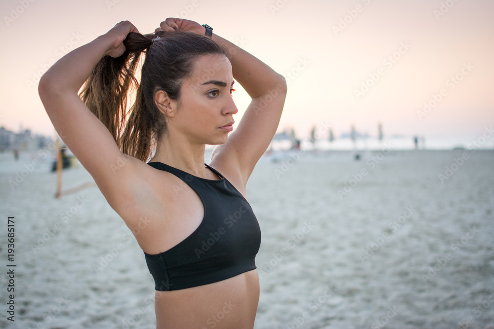 Beautiful sporty girl tying hair before her workout at beach. 