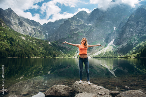 Young happy girl standing on the shore of the lake and admire the mountain scenery in Poland