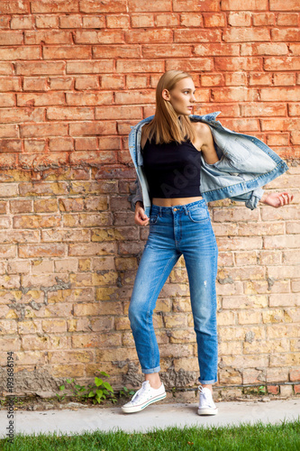 fashion girl standing near brick wall in denim and sneakers. Vogue Style