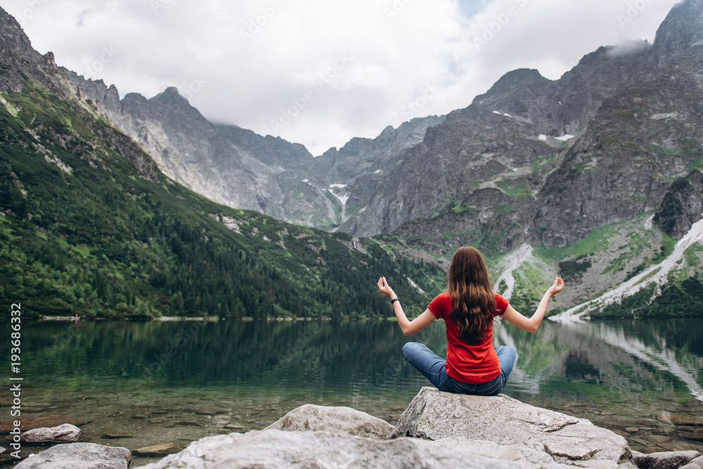 Fototapeta premium Young fitness woman meditating on the shore of the mountain lake