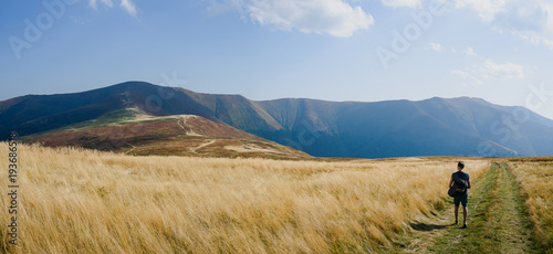 Man traveler admiring the panorama of the mountains that opened before him. Autumn landscape with dry grass. Road in the mountains. Borzhava Range, Carpathians, Ukraine, Europe