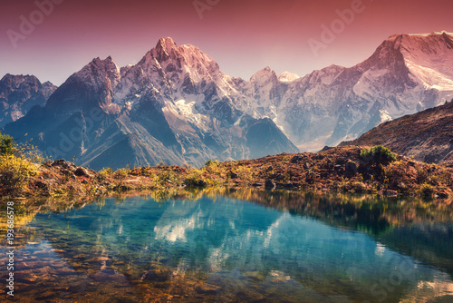 Beautiful landscape with high mountains with snow covered peaks, red sky reflected in lake. Mountain valley with reflection in water in sunset. Nepal. Amazing scene with Himalayan mountains. Nature photo