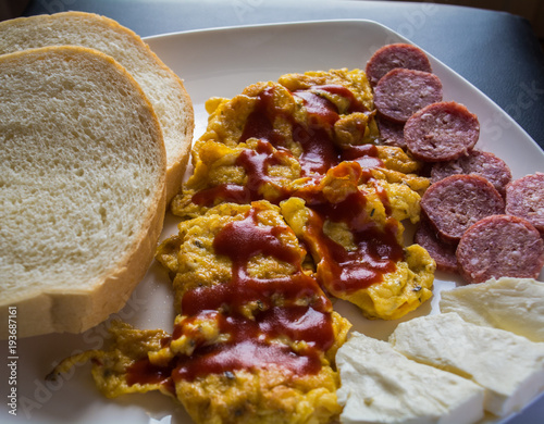 Scrambled eggs with ketchup with bread, salami  and cheese