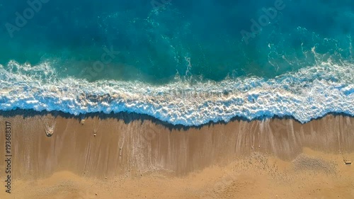 Aerial view looking straight down onto crashing waves hitting a golden beach