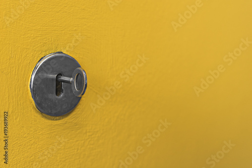 Grey metal keyhole against a bright yellow painted wall.