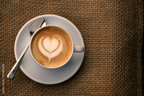 Tableau sur toile Cappuccino mit Milchschaum in Herzform in Tasse auf Hintergrund Sackleinen