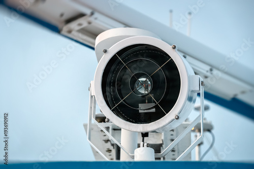 Searchlight on top of ship against the sky. Closeup.