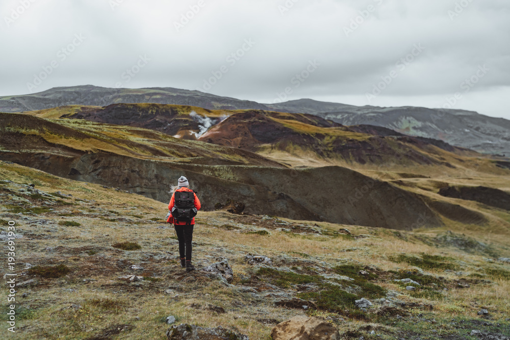 One woman wanders in Iceland with backpack in a red jacket