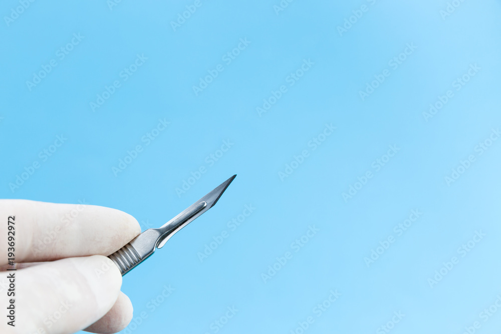 Scalpel in doctors hands in white medical gloves isolated on blue background copy space