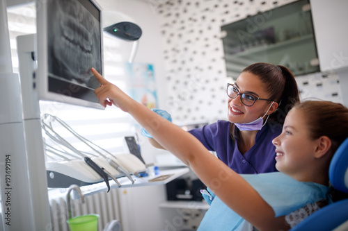 Girl in dental chair showing to dentist her tooth on dental x-ray