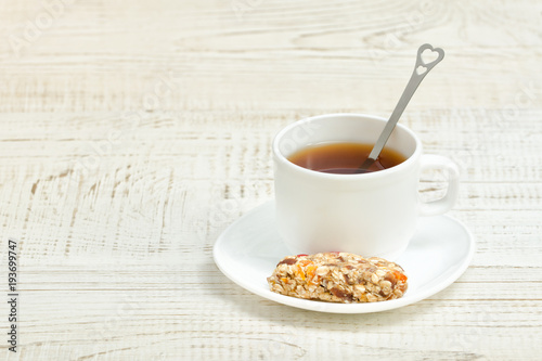 Cup of tea and a bar of muesli. White wooden background