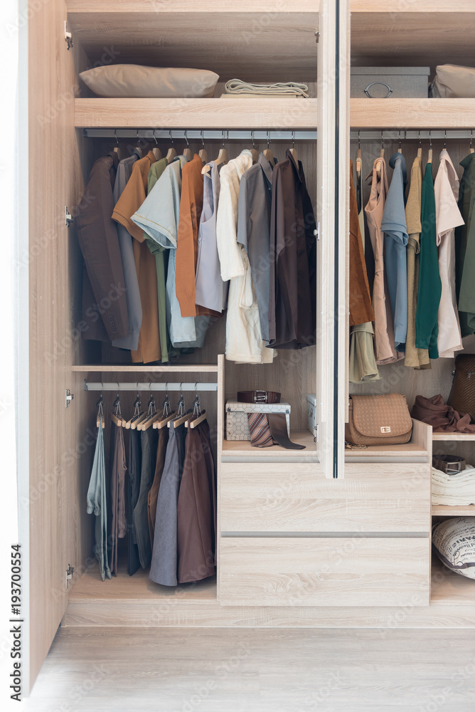 clothes hanging on rails in wooden wardrobe