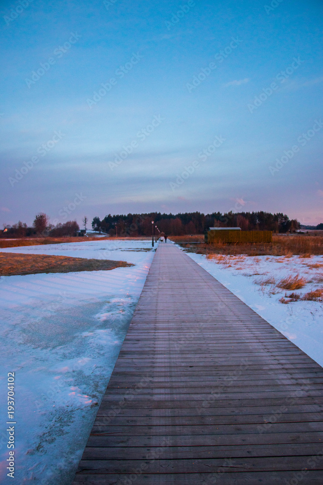 wooden bridge with snowy field at sunrise hour