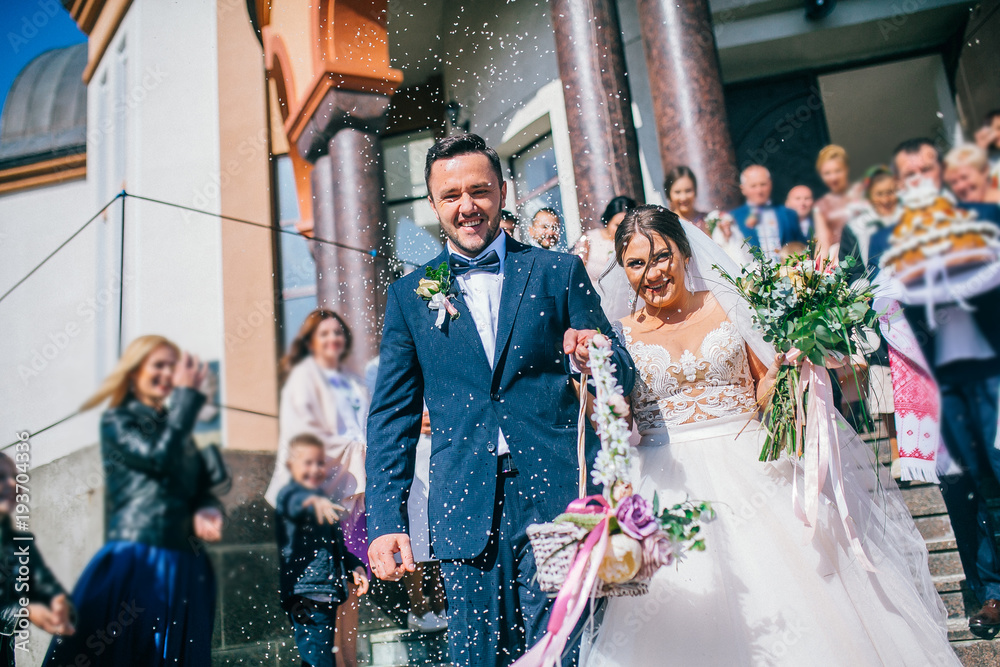 Guests Throwing Confetti Over Bride And Groom At Wedding. Newlyweds walking.