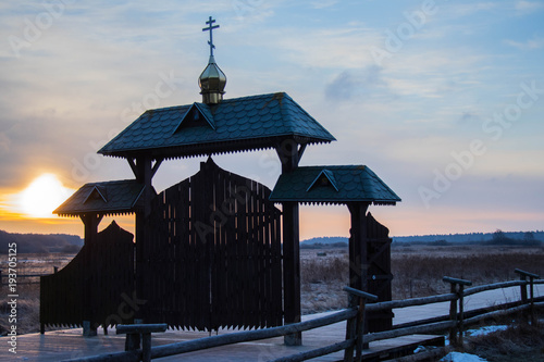 wooden traditional gate with domes and crosses leading to the Orthodox temple, set in the middle of fields and backwaters, seen in winter, at sunrise