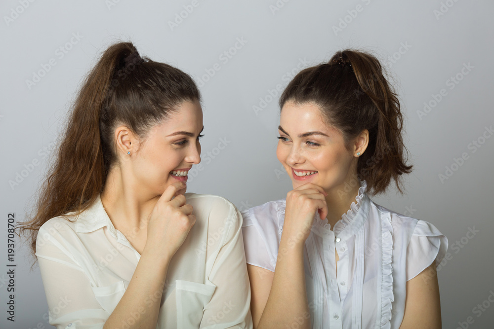 two beautiful smiling girl sisters twins in white blouses on a light background two beautiful smiling girl sisters twins in white blouses on a light background