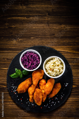 Fried chicken nuggets with cabbage served on black stone on wooden table