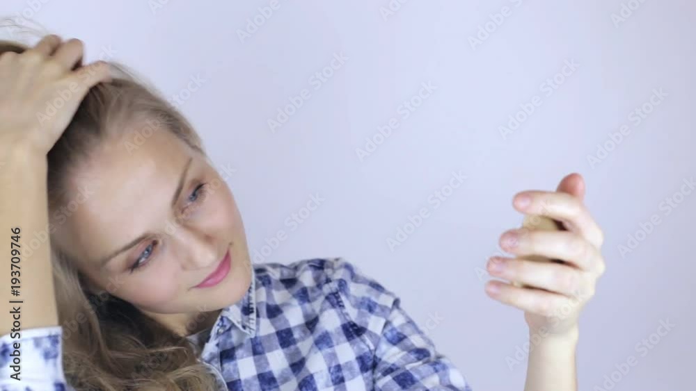 Beautiful girl straightens her hair and looking on little mirror Beautiful girl straightens her hair and looking on little mirror