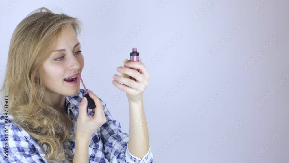 Beautiful model girl paints her lips looking on little mirror at home Beautiful model girl paints her lips looking on little mirror at home