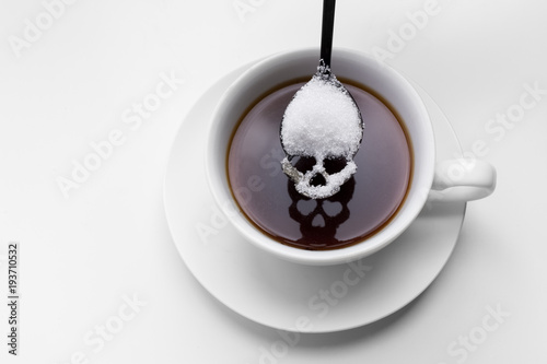 unhealthy white sugar concept. Scull spoon with sugar and cup of black coffee photo