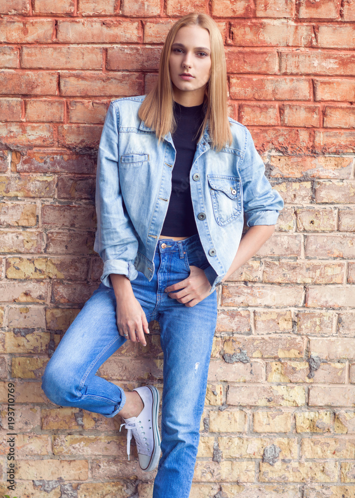 fashion girl standing near brick wall in denim and sneakers. Vogue Style