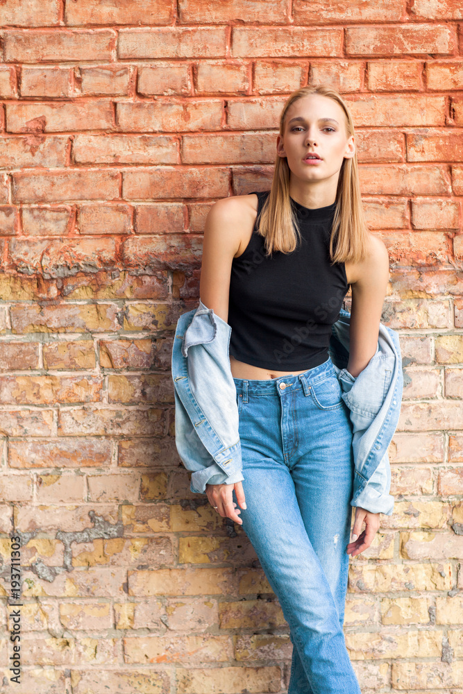 fashion girl standing near brick wall in denim and sneakers. Vogue Style