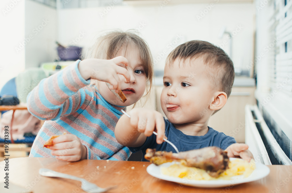 Children in the kitchen eat meat and mashed potatoes, very fun, share and feed each other Children in the kitchen eat meat and mashed potatoes, very fun, share and feed each other
