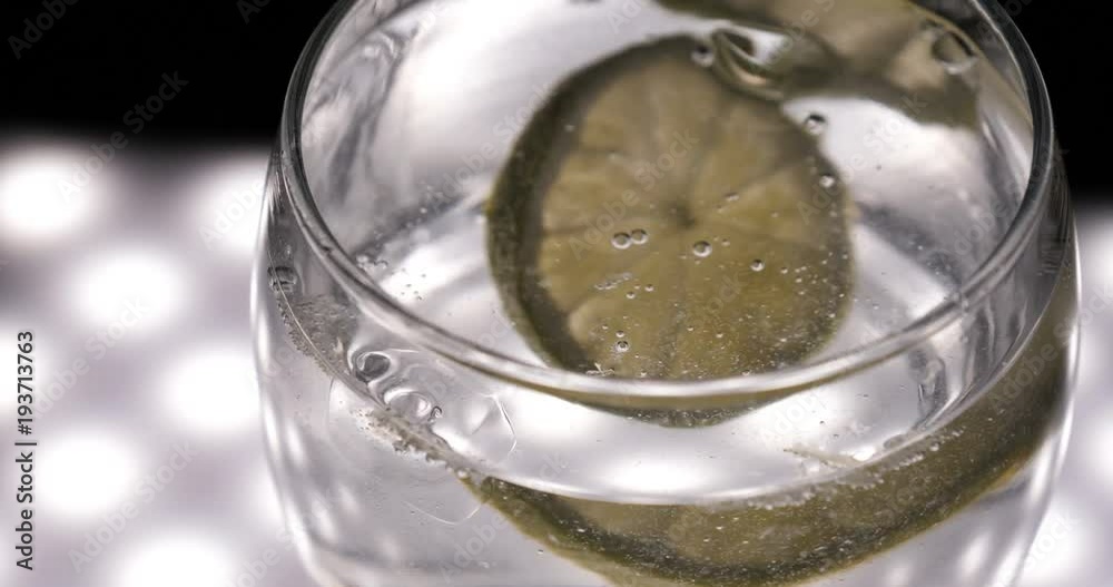Lemon, lime in a glass with soda water (bubbles), black background.