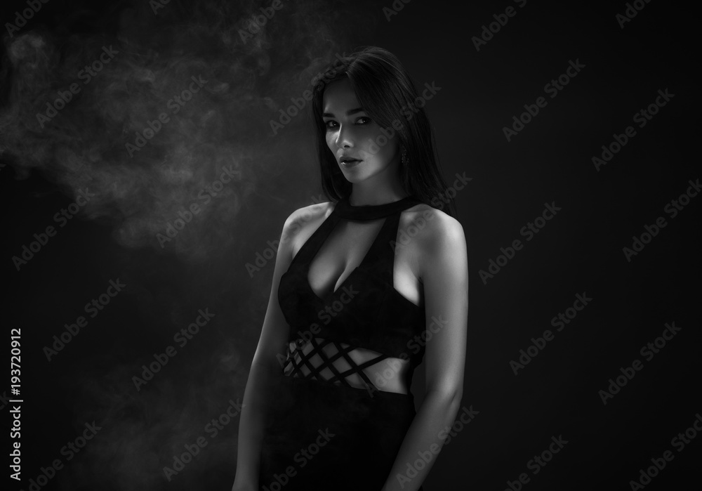 Beautiful girl in a black dress in the smoke. Dark background. Beautiful girl in a black dress in the smoke. Dark background.